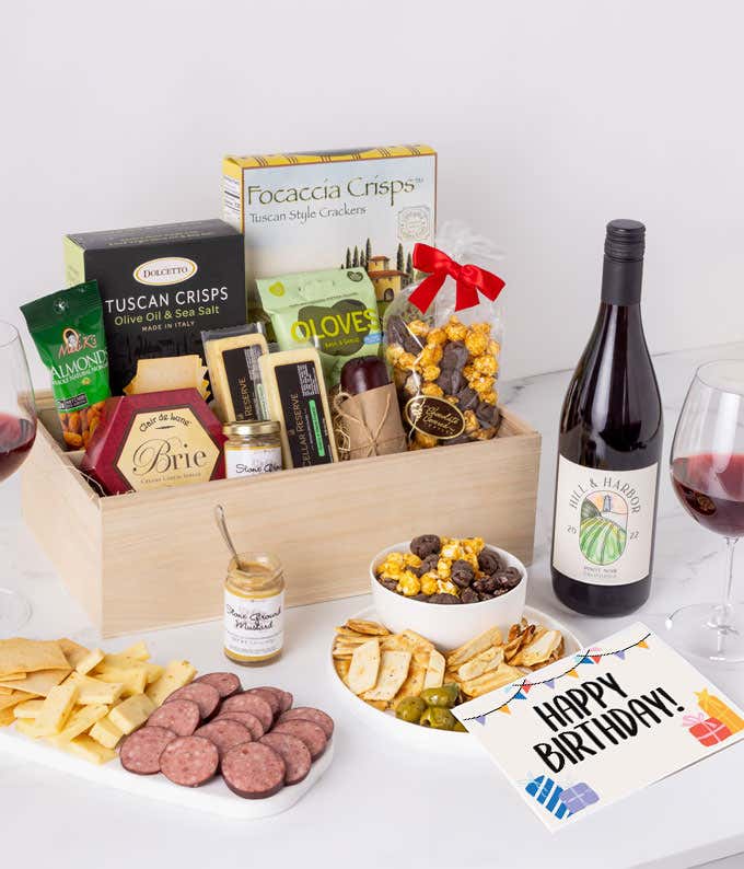 A charcuterie gift set with Tuscan crisps, focaccia crackers, 3 cheeses, summer sausage, olives, mustard, smoked almonds, chocolate-covered popcorn, and a birthday card.