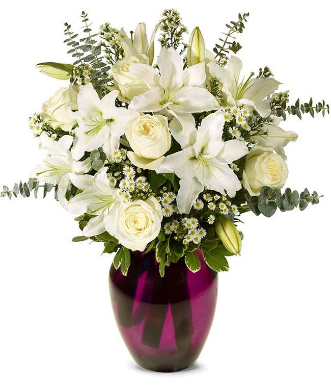 An elegant floral arrangement featuring white roses, white lilies, white asters, and eucalyptus, optionally displayed in a glass vase.
