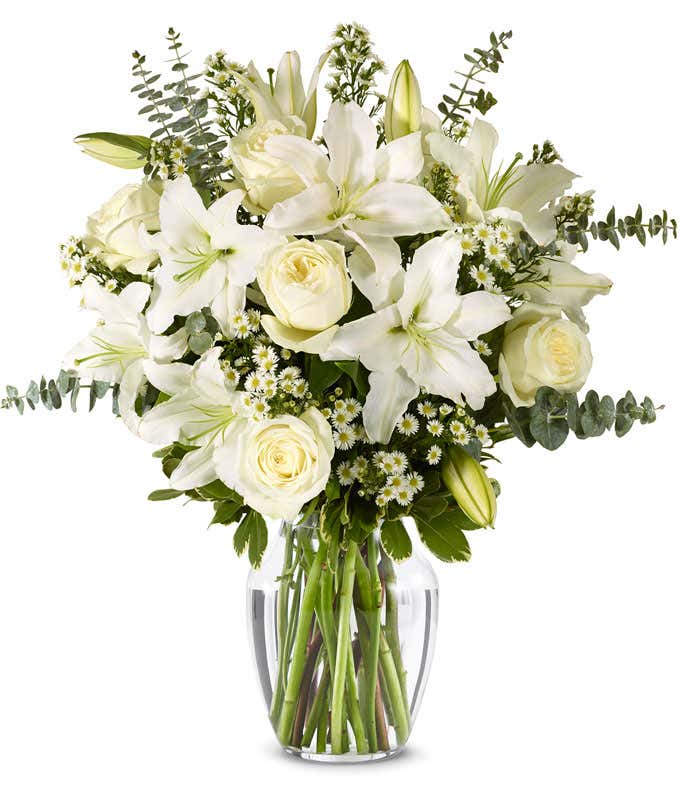An elegant floral arrangement featuring white roses, white lilies, white asters, and eucalyptus, optionally displayed in a glass vase.