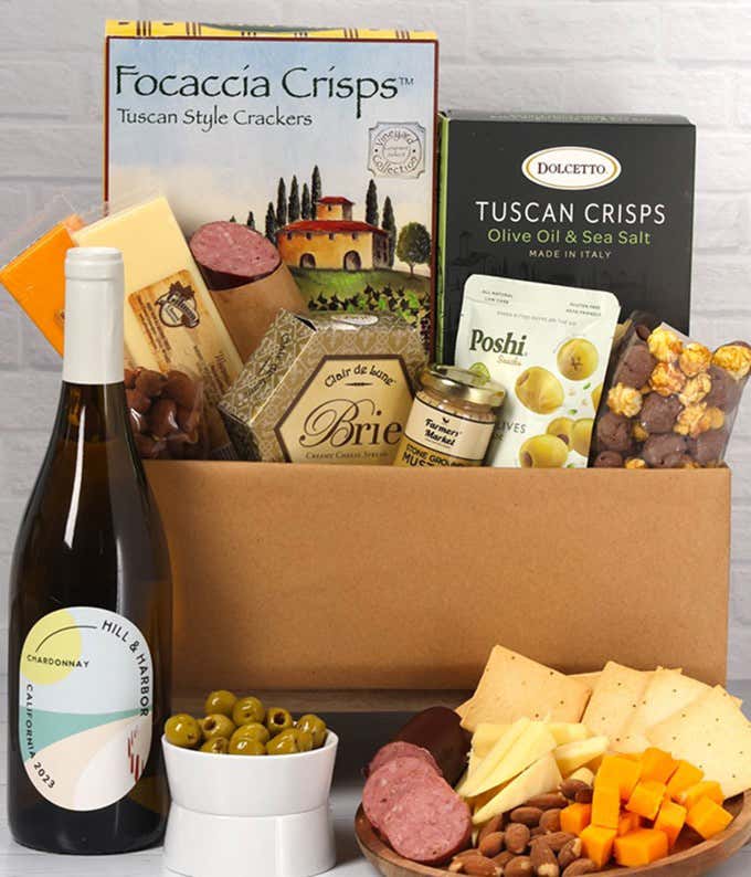 A charcuterie gift set with Tuscan crisps, focaccia crackers, 3 cheeses, olives, mustard, sausage almonds, chocolate-covered popcorn and a bottle of California Chardonnay.