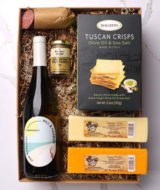 A gift box with a bottle of California Chardonnay, two types of cheese, crackers, stone-ground mustard, and a summer sausage.