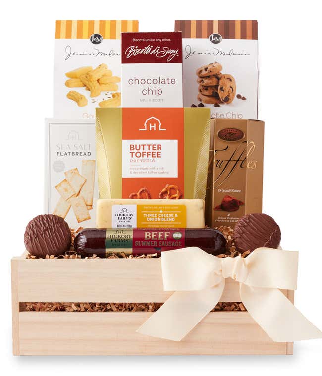 Gift crate filled with chocolate chip cookies, butter toffee pretzels, chocolate truffles, flatbread crackers, beef summer sausage, cheddar blend, and chocolate-covered sandwich cookies, with assorted treats arranged in front and tied with a cream bow.