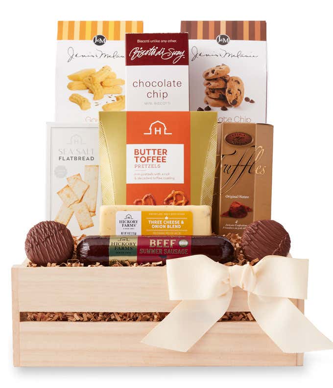Gift crate filled with chocolate chip cookies, butter toffee pretzels, chocolate truffles, flatbread crackers, beef summer sausage, cheddar blend, and chocolate-covered sandwich cookies, with assorted treats arranged in front and tied with a cream bow.
