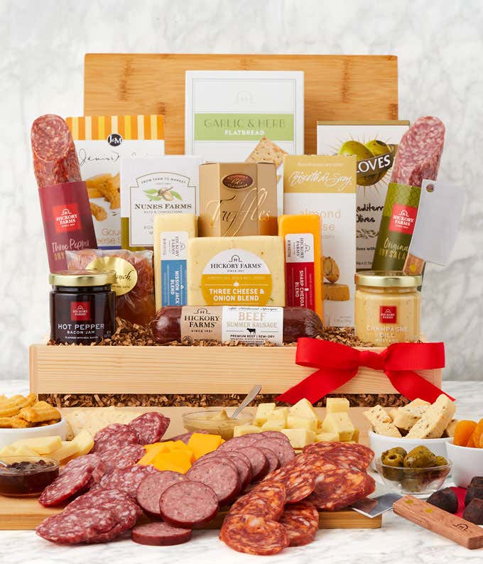 Gourmet charcuterie gift box with assorted salami, beef and turkey summer sausages, Three Cheese & Onion Blend, crackers, garlic & herb flatbread, hot pepper bacon jam, mustard, nuts, almond biscotti, and olives, arranged with a red bow.