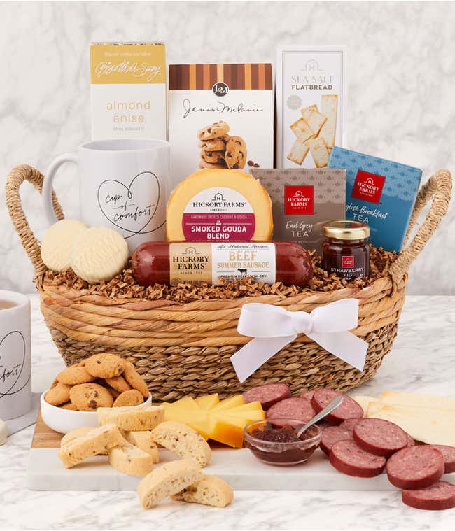 Sympathy gift basket in a woven tray with sausage, cheeses, flatbread, cookies, almond anise biscotti, tea, honey, two white mugs with &ldquo;Cup of Comfort&rdquo; design, and a white ribbon, displayed with a serving of meats, cheeses, cookies, and tea.