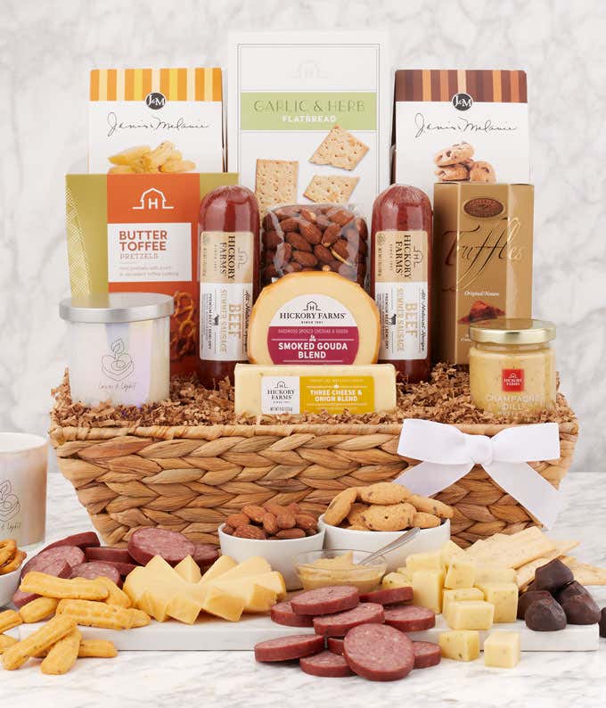 Sympathy gift basket in a woven tray with summer sausages, smoked gouda, cheddar blend, flatbread, cookies, truffles, toffee, mustard, and a white candle with a sympathy message, displayed with charcuterie-style spread of meats, cheeses, and treats.