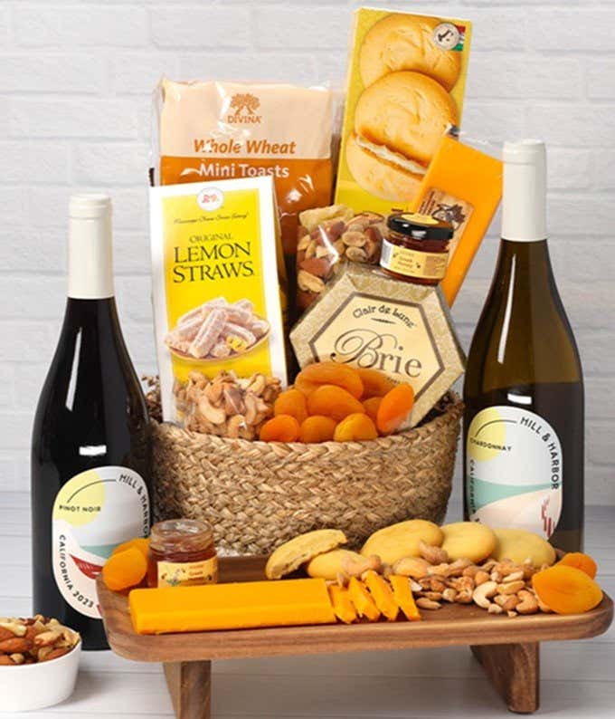 A two-toned woven basket filled with two cheeses, lemon flavored baked goods, crackers, dried apricots, gourmet nuts, and honey, paired with two bottles of wine - Chardonnay & Pinot Noir