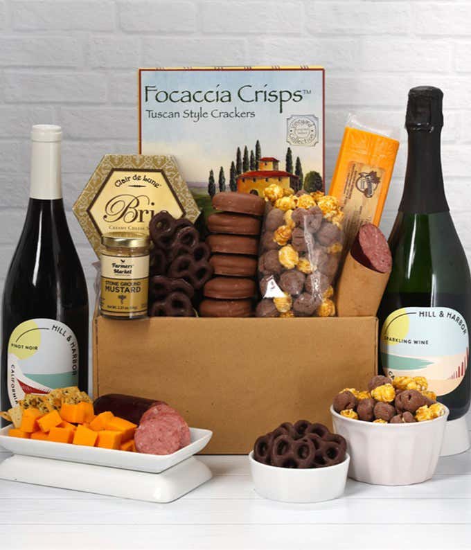 A gift set featuring 2 bottles of Hill & Harbor wine - red and sparkling, focaccia crisps, 2 cheeses, mustard, summer sausage, caramel popcorn, chocolate pretzels, and 6 chocolate-covered Oreos for a sweet and savory gourmet experience.